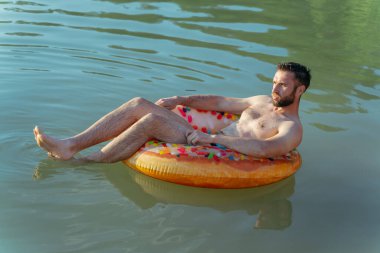 Dinlen. Bir adam göletteki şişme yüzükte yüzer..