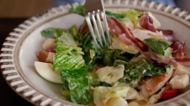 Salata. Bir kadının eli çatalla Sezar salatası karıştırıyor..