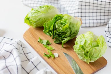 Mutfak havlularının yanındaki kesme tahtasının üzerinde üç yeşil marul salatası var. Sağlıklı yemek teması.