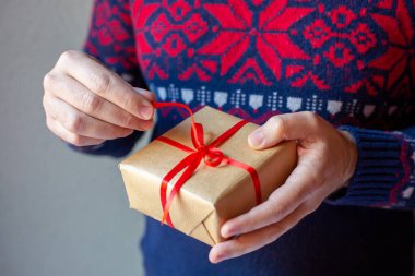Yılbaşı desenli süveter giyen bir adam gri arka planda bir Noel hediyesi tutar. Noel ve Yeni Yıl için hediye konsepti.
