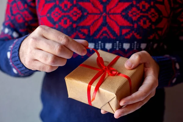 Yılbaşı desenli süveter giyen bir adam gri arka planda bir Noel hediyesi tutar. Noel ve Yeni Yıl için hediye konsepti.