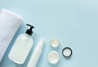 Spa ve doğal kozmetik teması. Beyaz kavanozlarda organik kozmetik seti, beyaz banyo havlusu ve mavi arka planda. Mesaj için boş yer var..