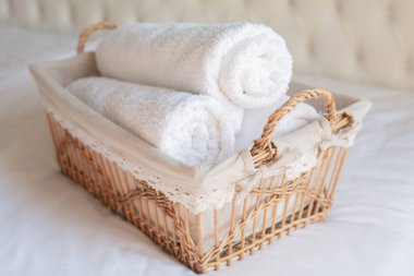 Beyaz arka planda hasır bir sepette üç rulo beyaz havlu var. Retro biçimi.