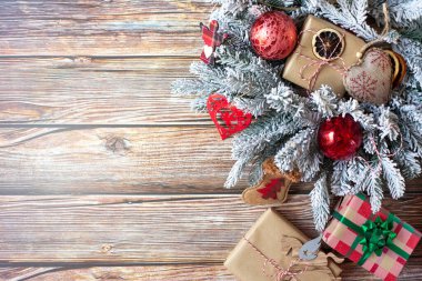 Karda Noel süsleri ve paketlenmiş hediye kutularıyla süslenmiş dallar ahşap bir arka planda. Metin için boş alan.