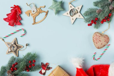 Mavi arka planda kırmızı böğürtlen ve süslemeli Noel köknar dalları var. Yeni yıl teması üzerine çerçeve şeklinde bir arkaplan. Ortadaki metin için boş alan. En üstten görüntüle.