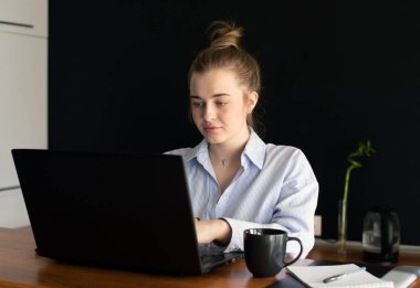 Genç bir kadın evdeki ya da ofisteki mutfakta otururken defter üzerinde çalışıyor. İnternetten öğrenim görme ya da çalışma kavramı.