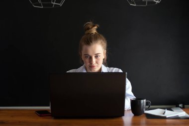 Genç bir kadın evdeki ya da ofisteki mutfakta otururken defter üzerinde çalışıyor. İnternetten öğrenim görme ya da çalışma kavramı. Dikey resim.