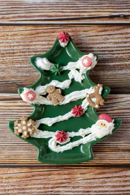 Noel ağacı şeklinde pasta kremi ve diğer süslemelerle süslenmiş tabaklar ahşap bir arka planda. Dikey fotoğraf. 
