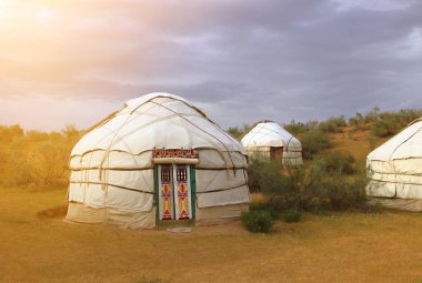 Birçok geleneksel Asya yurdu gün batımında gün ışığıyla aydınlanan bozkırda duruyor..