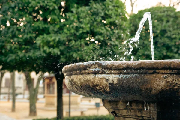An ancient fountain with flowing water in a blurred focus against the background of a city street.