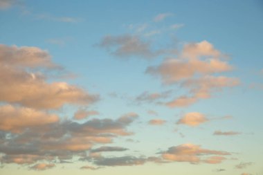 Akşam güneşiyle aydınlanan turuncu bulutlu mavi gökyüzü.