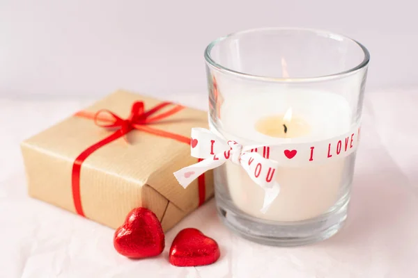 テーマはバレンタインデー 心の形をした燃えるろうそくと2つの赤いキャンディーとパックされた贈り物は白い背景にあります テキストのためのフリースペース — ストック写真