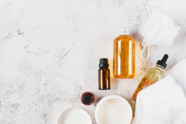 Kaplıca ve güzellik. Gri arka planda bir takım kozmetik ürünler, bir şişe doğal yağ ve beyaz havlu var. Metin için boş alan. En üstten görüntüle.