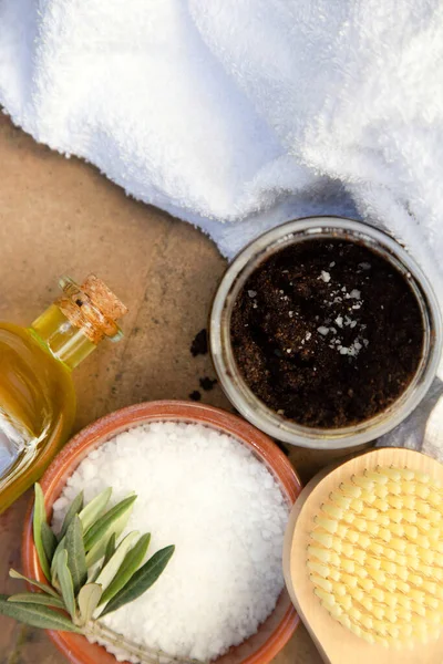 A jar of handmade coffee scrub, sea salt, body brush with olive oil are on a brick background. View from the top point. Free space for text.
