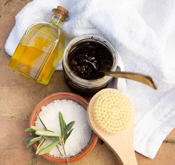 A jar of handmade coffee scrub, sea salt, body brush with olive oil are on a brick background. View from the top point. Free space for text. A square image.