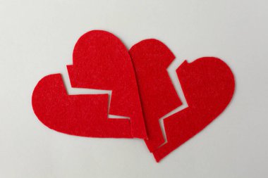 Kırmızı renkte iki kırık kalp gri arka planda yan yana yatar. Aşkın sembolü olarak kalbin teması.