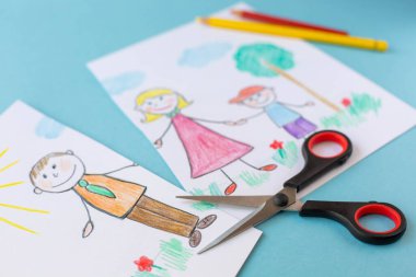 Scissors lie on a cut children's drawing depicting a family. The topic of divorce of spouses.