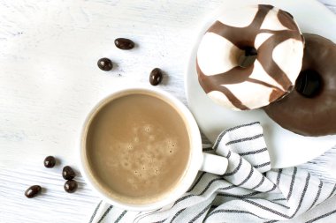 Masanın üzerinde beyaz bir fincan espresso ve çikolatalı çörek var. En üstten görüntüle.