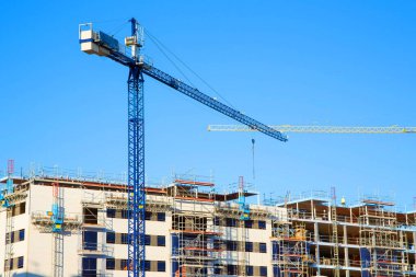 Çatıda inşaat halindeki bir bina ve mavi gökyüzüne karşı duran vinçler..