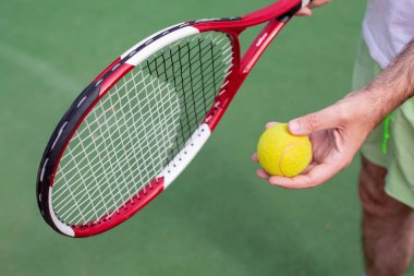 A man in one hand holds a racket and the ball in the other hand stands on a tennis court. The theme of sports and a healthy lifestyle.