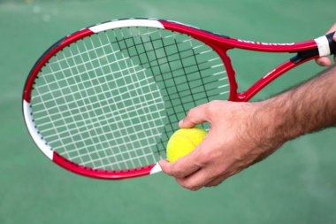 In the men's hands are a tennis racket and a ball against the background of a tennis court.