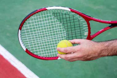 In the men's hands are a tennis racket and a ball against the background of a tennis court.