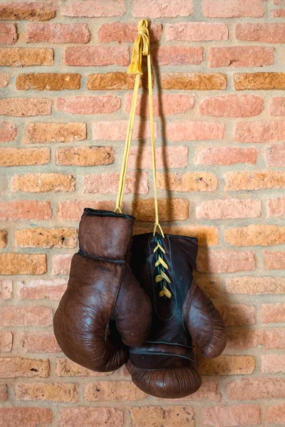 A pair of vintage boxer leather gloves hang against a brick wall. Retro style. A vertical image.