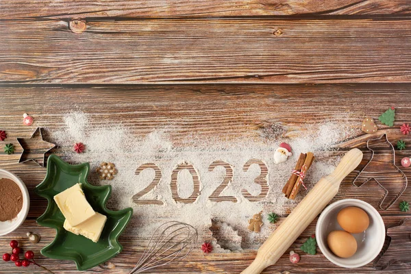 Yeni yıl pişirme teması. Ürünler, mutfak gereçleri ve 2023 numaraları ahşap arka planda. Uzayı kopyala En üstten görüntüle.