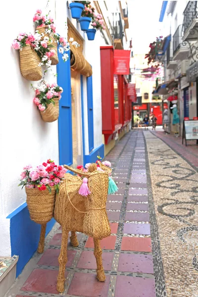 手前には花で飾られたお店や藁で作られたロバの姿が美しい通り スペインのマルベージャの地中海の町の通り — ストック写真