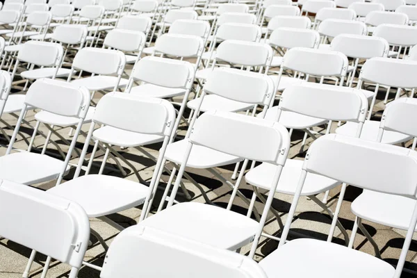 White plastic chairs for a concert, wedding or business conference stand in rows on the street. Folding chairs stand in a row for a public event in the city.