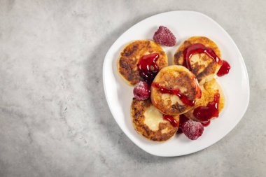 Açık gri arka planda beyaz tabakta ahududu ve şuruplu kremalı börek, seçici odak