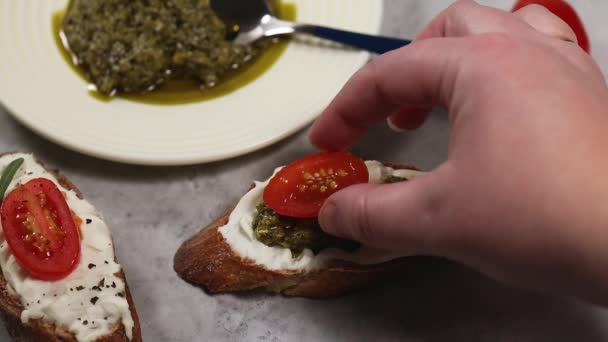Kanapki gotowania w domu, ręcznie umieścić plasterek pomidora wiśniowego na plasterek chleba z serem wiejskim i sosem pesto — Wideo stockowe