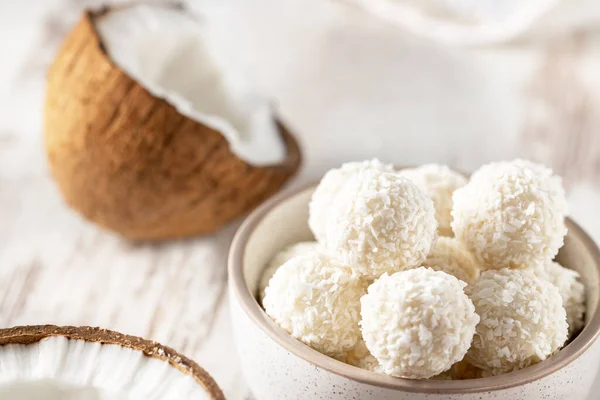 Caramelle dolci al cocco in ciotola, cocco rotto su fondo chiaro, messa a fuoco selettiva — Foto Stock