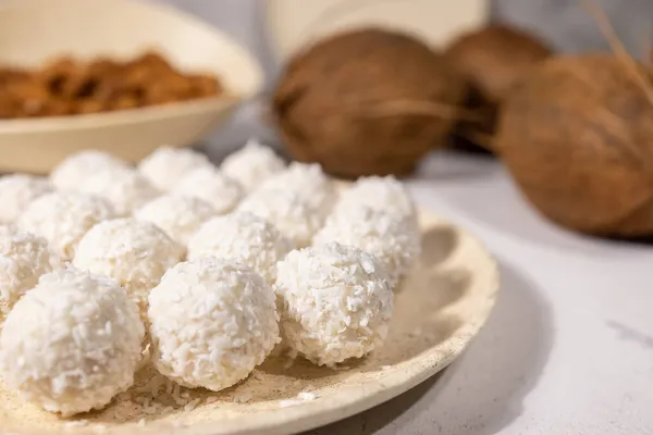 Bílé sladké kokosové bonbóny v talíři, kokosové ořechy a mandlové oříšky na pozadí, zblízka se selektivním zaměřením — Stock fotografie