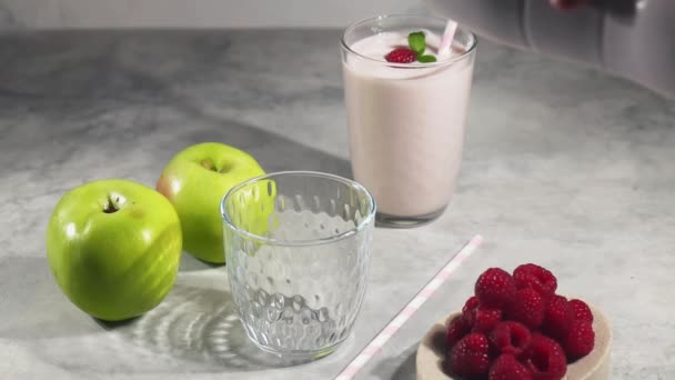 Giet fruityoghurt in glazen beker, appel- en frambozenmilkshake, yoghurtdrank en ingrediënten op tafel — Stockvideo