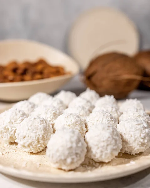 Bílé sladké kokosové bonbóny v talíři, kokosové ořechy a mandlové oříšky na pozadí, zblízka se selektivním zaměřením, vertikální — Stock fotografie