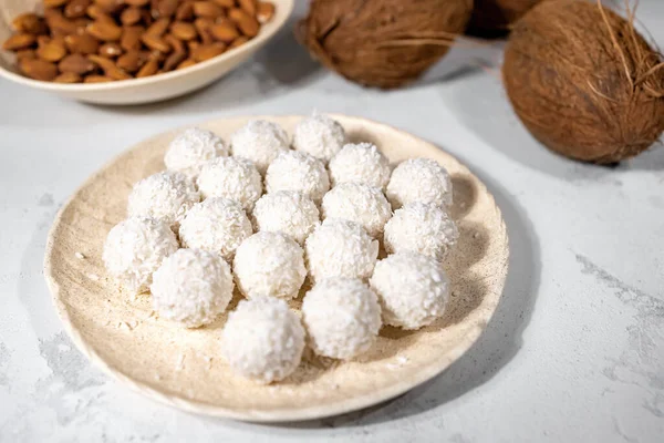Bílé sladké kokosové bonbóny v talíři, kokosové ořechy a mandlové oříšky, ingredience na pozadí, zblízka s výběrovým zaměřením — Stock fotografie