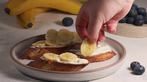 Przygotowując śniadanie owocowe, kobieta wkłada plasterek banana na kanapkę z serem śmietankowym, zamyka — Wideo stockowe