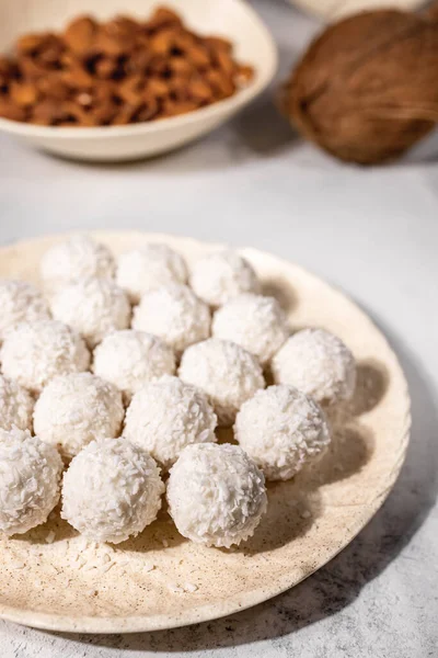 Bílé sladké kokosové bonbóny v talíři, kokosové ořechy a mandlové oříšky na pozadí, selektivní zaměření, vertikální — Stock fotografie