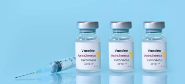 Harkiv. Ukrayna. 9 Ocak 2021. Şırınga, üç şişe koronavirüs aşısı mavi arka planda AstraZeneca logosu. Tıp, sağlık, bilim konsepti. Üç doz. Metin için alan kopyala.