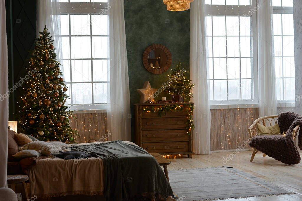 Interior of a beautiful Christmas bedroom with a wooden bed, armchair, chest of drawers ,beautifully decorated Christmas tree by the window. Christmas decorations. Happy New Year and Merry Christmas!