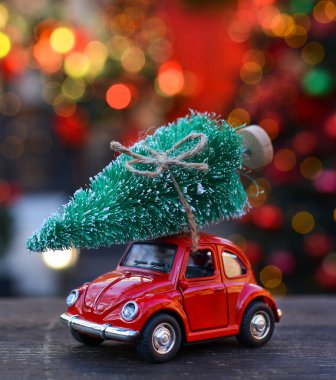 Oyuncak kırmızı araba Noel Bokeh 'in arka planında küçük bir Noel ağacı taşıyor. Noel kartları. Kamyon. Teslimat servisi.
