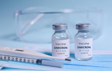 Omicron Varyasyon Coronavirus, şırınga, yüz maskesi, vücut termometresi ve koruyucu gözlüklere karşı bağışıklık kazandırmak için iki şişe Covid-19 aşısı.