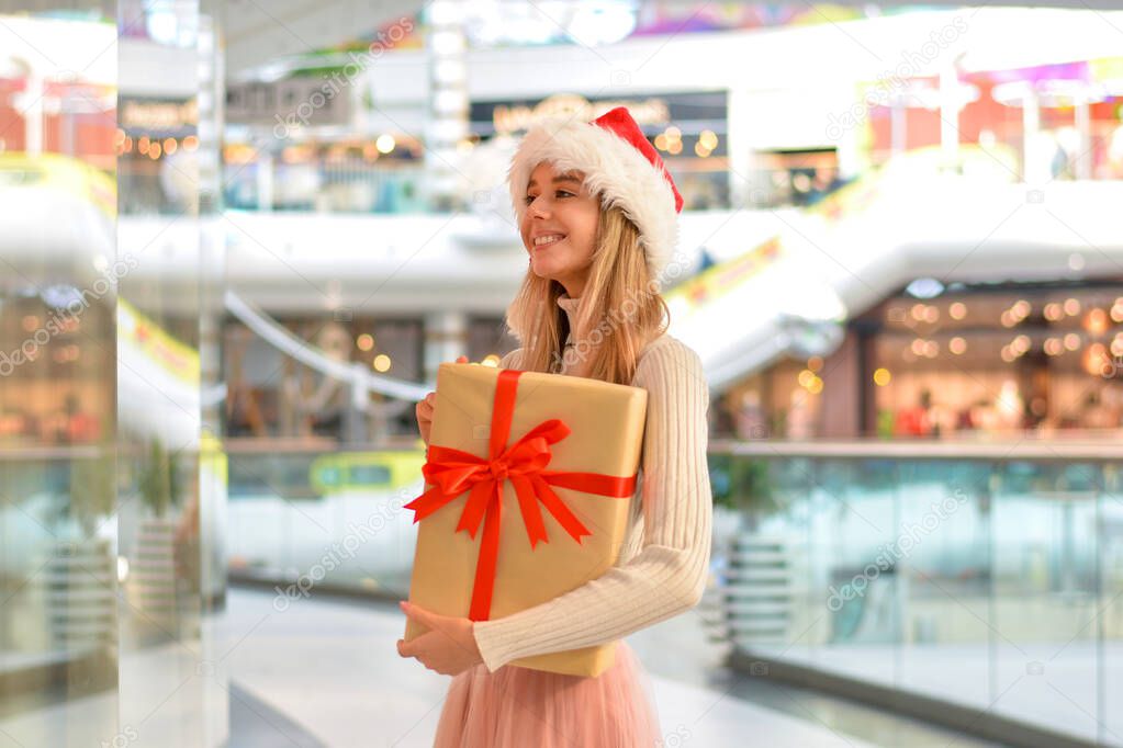 Happy Young woman in santa hat with gift box in the Shopping Mall. Holiday shopping and gifts.Shopper. Sales. Shopping Center