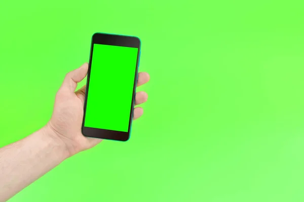 A man holds a smartphone with a green screen on green background.Mockup. Copy space for text
