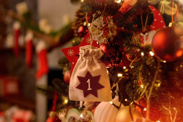 Advent calendar in the form of an eco bag hangs on the Christmas tree against the background of the Christmas room with a fireplace and Santa\'s boots.Christmas background. Advent calendar.