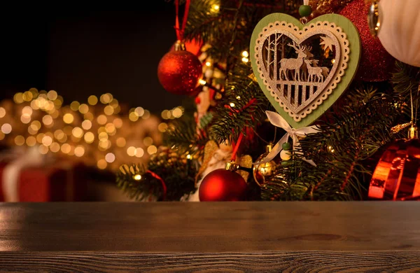 Empty wooden table on the background of a Christmas tree with beautiful toys in the form of balls, a wooden heart with deer, garlands and fireplace with golden bokeh. Christmas background. .Mockup