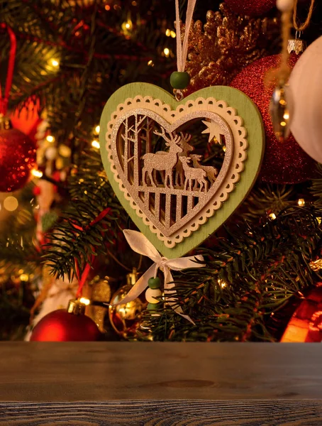Empty wooden table on the background of a Christmas tree with beautiful toys in the form of balls, a wooden heart with deer, garlands. Ready for product montage.Mockup. Merry Christmas !