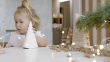 Masada Noel süsleri ve ağaç dallarıyla küçük şirin bir kız oturuyor. Noel kurabiyesi. Yılbaşı şekerleri Noel ağacının dalları.