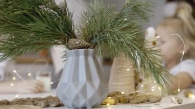 Masada Noel süsleri ve ağaç dallarıyla küçük şirin bir kız oturuyor. Noel kurabiyesi. Yılbaşı şekerleri Noel ağacının dalları.